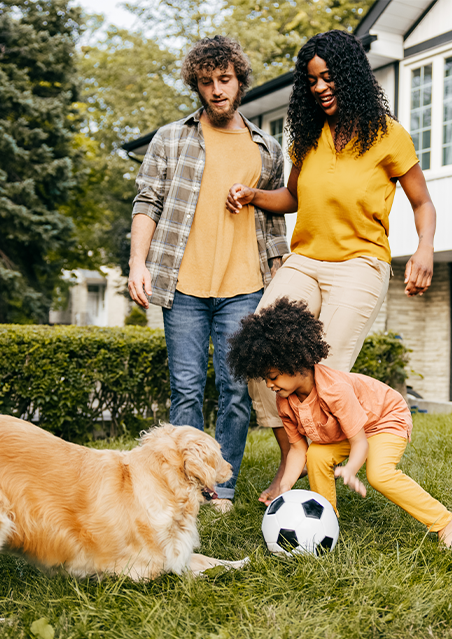 Family playing soccer outside home with pet