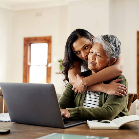 woman hugging her grandmother and looking at a laptop