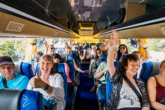 Group on tour bus smiling with thumbs up