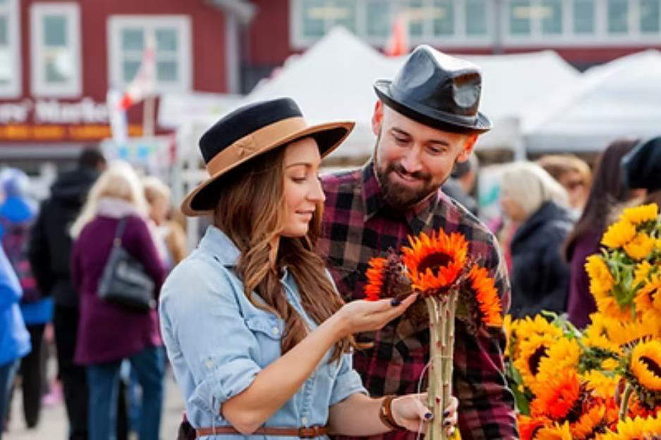 couple looking at sunflowers being sold at a booth outside at the St Jacobs Farmers Market on a summer day