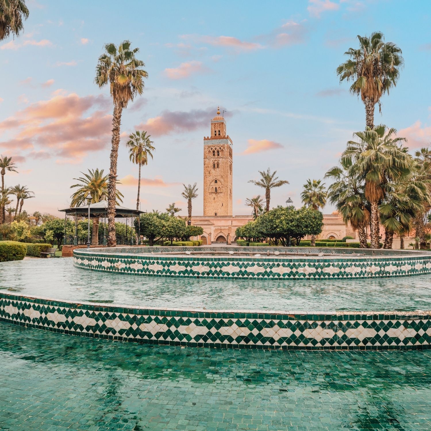 The majestic Koutoubia Mosque rises above a serene fountain in Marrakech, Morocco, bathed in the warm glow of the setting sun