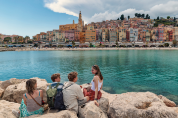 tourists sitting on stone breakwater jetty looking at the beautiful townscape of colorful buildings of Menton
