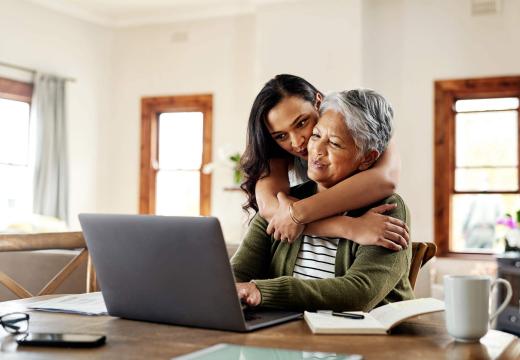 woman hugging her grandmother and looking at a laptop