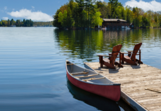 Two Adirondack chairs on a wooden dock overlook the waters of a Muskoka lake in Ontario, Canada