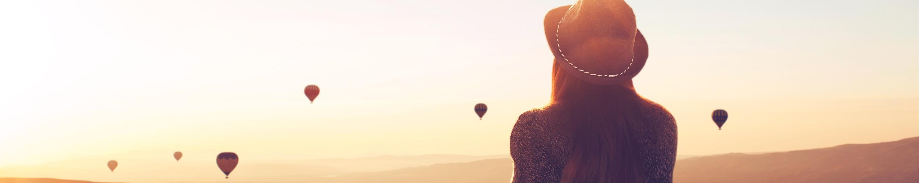 girl sitting on a hill and looking at air balloons