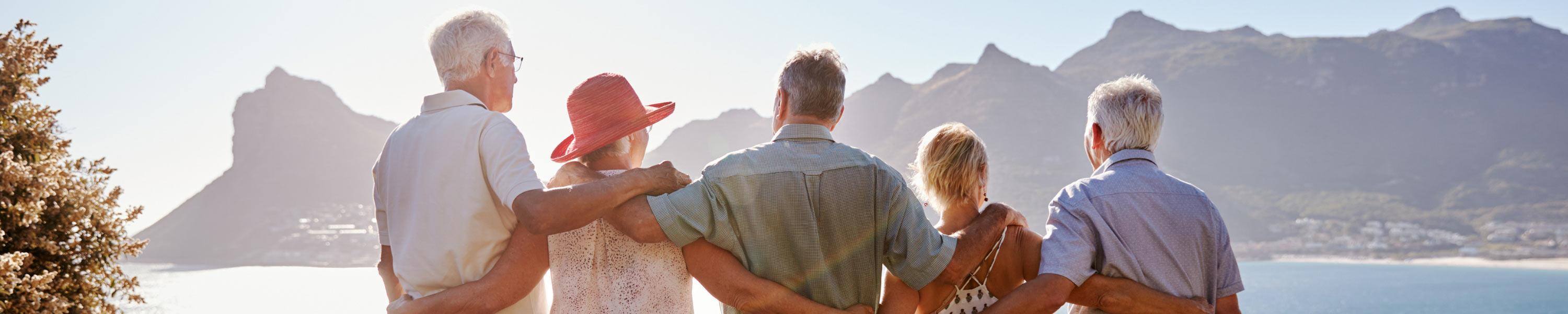 Rear View Of Senior Friends Visiting Tourist Landmark On Group Vacation Standing On Wall