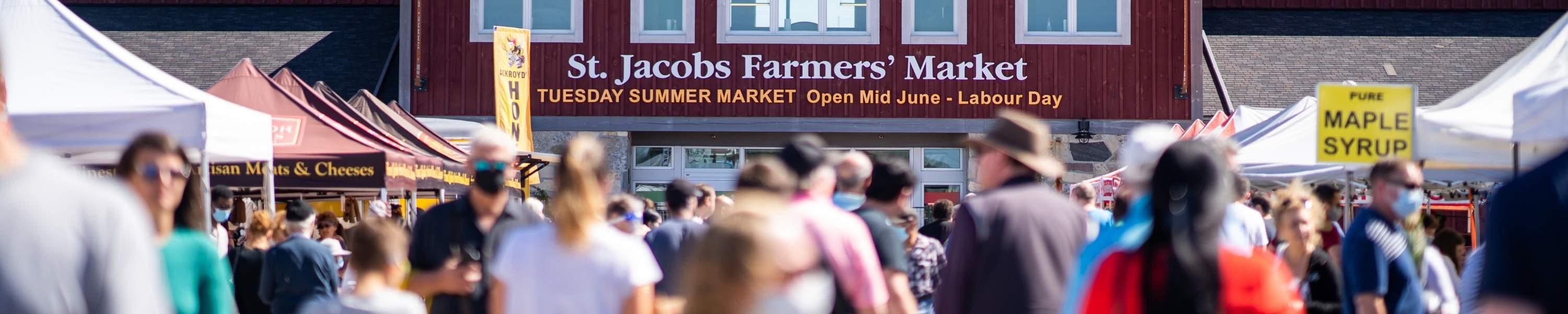 outside of the st jacobs farmers market with many shoppers shopping at booths outside on a sunny day