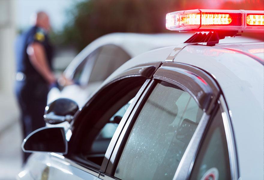 A police officer stands next to a car he pulled over for speeding, reaching for the driver's ID.