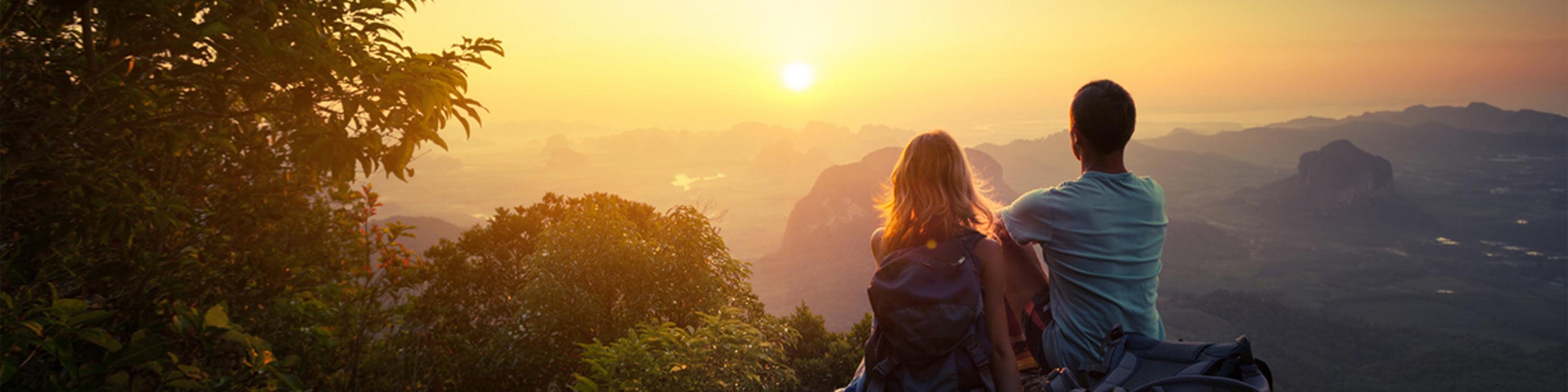 Two hikers on top of the mountain enjoying sunrise over the tropical valley